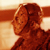 Pixelated static image of a character's head and shoulders in warm brown tones with visible dithering and low-resolution rendering.