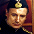 Pixelated portrait of a person wearing a dark uniform with gold trim and a golden emblem on the head, set against a dark background with red and brown elements.