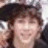 Pixelated static image of a person with brown hair and light skin, wearing dark clothing against a blurred background.