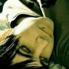 A close-up of a person with dark hair lying down, wearing a light-colored top with dark stripes, against a green background.