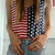 A person in a red and white striped top with blue checkered sleeves stands against a light background, hands clasped at waist level.