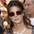 A pixelated close-up of a person with dark hair wearing red-tinted sunglasses and a white top, holding a golden trophy-like object.