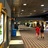 Pixelated image showing a dimly lit indoor space with multiple figures, a vertical light fixture on the left, and a patterned floor.