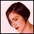 Pixelated static image of a person's head and shoulders with dark brown hair, light skin tone, and visible facial features against a pale pink background.
