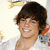 A person with brown hair wearing a white shirt, smiling broadly against a light background with partial red and blue elements.