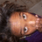 Pixelated close-up of a person's face with light skin tone, dark hair, and large eyes, set against a dark background with purple and brown tones.