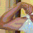 Pixelated static image of a figure in motion with flowing pink and brown hair, wearing a light-colored garment against a patterned background.