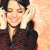 Pixelated close-up of a person with dark hair wearing a dark red zippered jacket, smiling and holding hands near the face against a light background.