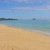 A static beach scene with sandy shore, turquoise water, and distant dark landmass under blue sky.