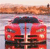 Red vehicle with dark roof and headlights, positioned on a reflective surface under a gradient sky.