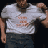 A person in a white t-shirt with orange text and dark shorts appears in three sequential poses against a black background, showing arm movements.