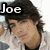Pixelated image of a person with dark hair wearing a white shirt, featuring the text 'Joe' in bold black and white lettering at top left.