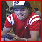 Pixelated image of a person in a red shirt with white stripes, wearing a dark cap, next to a red-bordered sign with text.