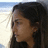 Pixelated close-up of a person with dark hair and brown skin, profile view facing left, against a light background with blue sky.