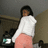Pixelated image of a person in white top and pink pants holding a black lantern with green light, standing against dark background.