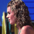 Pixelated close-up of a person with curly brown hair holding a microphone against a blue background.