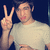 A person in a light-colored shirt makes a peace sign with their right hand against a dark background, next to bold text reading PEACE!