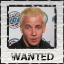 Static 64x64 pixel buddy icon featuring a person with short blonde hair in a black shirt against a light background, framed by a border with "WANTED" text at the bottom and partial blue circular shapes on the left side.
