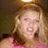 Pixelated close-up of a person with light brown hair wearing a pink top against a dark background.