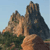 Pixelated landscape showing rocky mountain peaks with a light blue sky background and green foliage at the base.