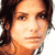 Pixelated static image of a person's face with dark hair and light skin tone, rendered in warm orange-brown color palette on white background.