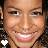 A pixelated close-up of a smiling person with light brown skin, dark eyes, and visible teeth; the background is blurred.