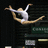 A pixelated gymnast in mid-air pose with arms and legs extended, wearing a white leotard against dark background.