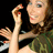 A pixelated close-up of a person with long brown hair wearing a green garment, raising a hand with red-painted fingernails against a black background.
