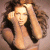 Static pixelated image of a person with long dark hair and light skin, wearing a sleeveless top in warm tones against a neutral background.