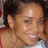 A person with short dark hair and a light brown skin tone smiles while wearing a white top with a red strap visible on the shoulder.