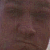 Pixelated close-up of a person's face with dark hair and brown skin tone, showing eyes, nose, and mouth in low-resolution detail.