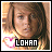 Pixelated image of a person with brown hair and light skin, wearing a white top with pink accents, against a warm-toned background.