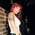 A woman with red hair and a tattoo on her upper arm stands against a brick wall, wearing a white tank top and dark pants, with a slight shift in posture across frames.