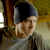 Static pixelated image of a person wearing a dark cap and light-colored shirt against a blurred background with warm tones.