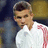 Pixelated image of a person with short dark hair wearing a white shirt and gray jacket, standing against a blurred background.