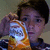 A person holds an orange and white snack bag with visible text, positioned near their face across four
