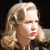 Pixelated close-up of a person with light brown hair holding a microphone, red lips, and a dark background.