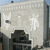 Static pixelated image of a light-colored building facade with dark architectural details and a blue sky background.