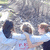 Three people in light blue shirts embrace outdoors with a rocky background; red text appears on the front of one shirt.