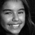 Black-and-white pixelated portrait of a smiling person with dark hair, cropped to show face and upper shoulders against solid black background.