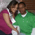 Two people in close embrace, one wearing a green sweater over white shirt and dark pants, the other in magenta top with white trim; background shows brick wall.