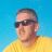 Pixelated static image of a person wearing dark sunglasses and a yellow shirt against a blue background.