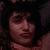 Pixelated close-up of a person's face with dark hair against a black background, showing partial facial features and clothing.