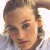 Static pixelated image of a person with light brown hair styled in an updo, wearing a white collared shirt against a bright background.