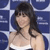 Pixelated image of a person with dark shoulder-length hair wearing a white strapless top against a blue grid background.