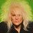 Pixelated static image of a person with long blonde hair wearing dark clothing against a green and yellow gradient background.