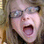 A pixelated close-up of a person with light brown hair and glasses, mouth open in an exaggerated expression, blue text at bottom reads 'nerdy giggles'.