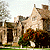 Pixelated static image of a stone building with multiple chimneys and a dark doorway, surrounded by trees and greenery under a light sky.