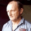 A man in a light blue collared shirt with a red emblem on the chest appears in a of showing slight variations in head position and facial expression