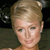 Static pixelated image of a person with short light brown hair styled upward, wearing a small earring, against a dark background with blurred shapes.